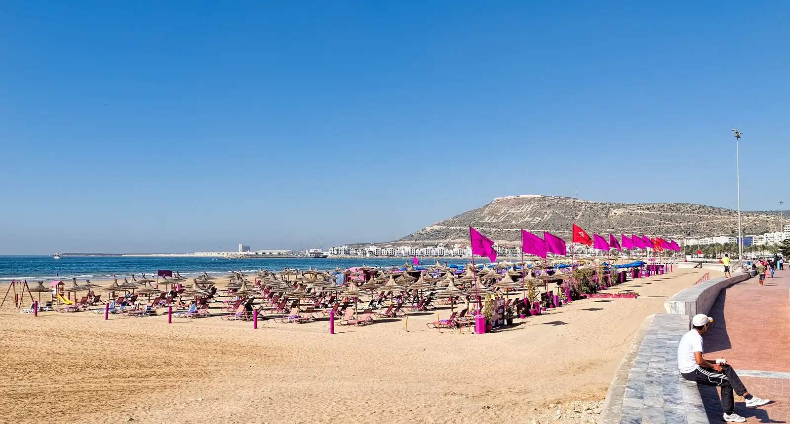 Agadir beach with parasols and the kasbah hill of Agadir Oufella under a clear blue sky